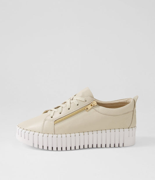 Beige sneaker with a gold zipper on a light gray background