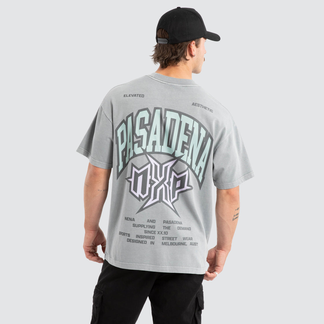 Person wearing a gray t-shirt with 'Pasadena' text and logo on the back, standing against a white background.